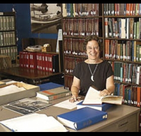 Joan Berman at a desk reviewing papers with bookshelves behind her