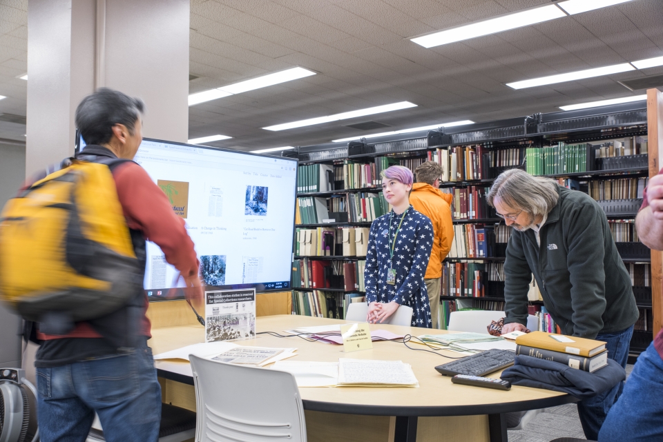 student standing by table presenting on large screen