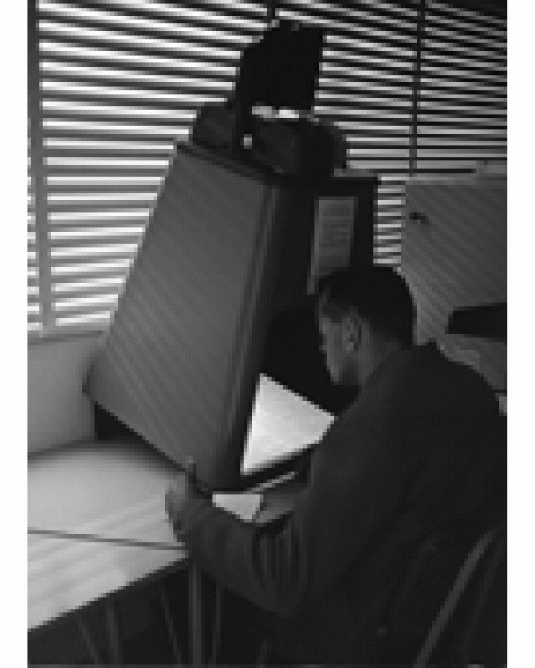 black and white photography of a man sitting in front of an old microfilm reader