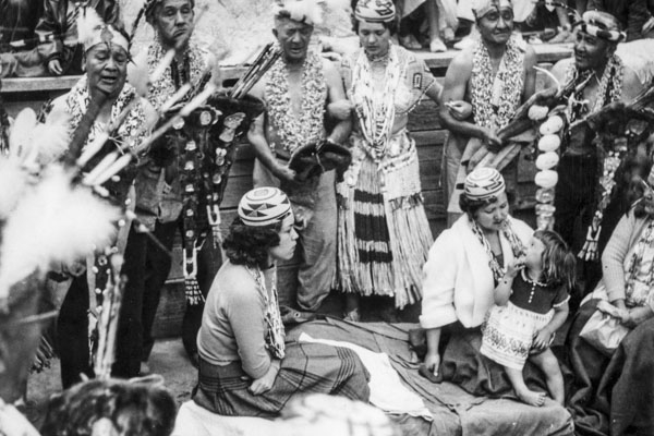 black and white image of Native American women and children surrounded by others in traditional dress